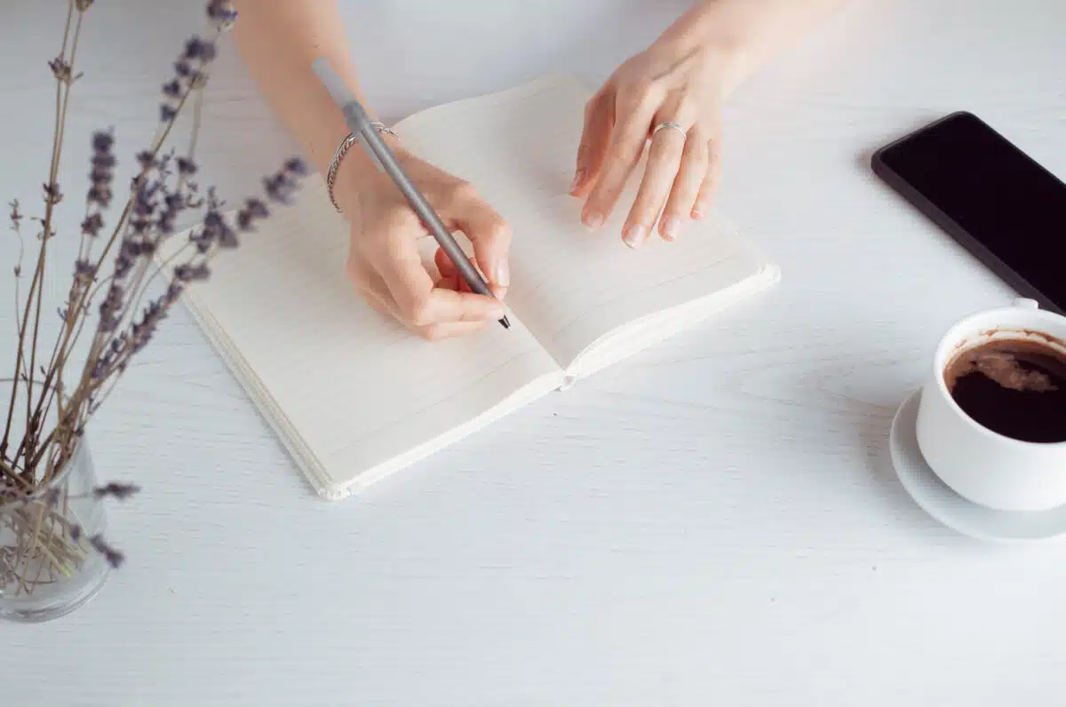 Woman's hands are writing in a notebook while sitting at home.