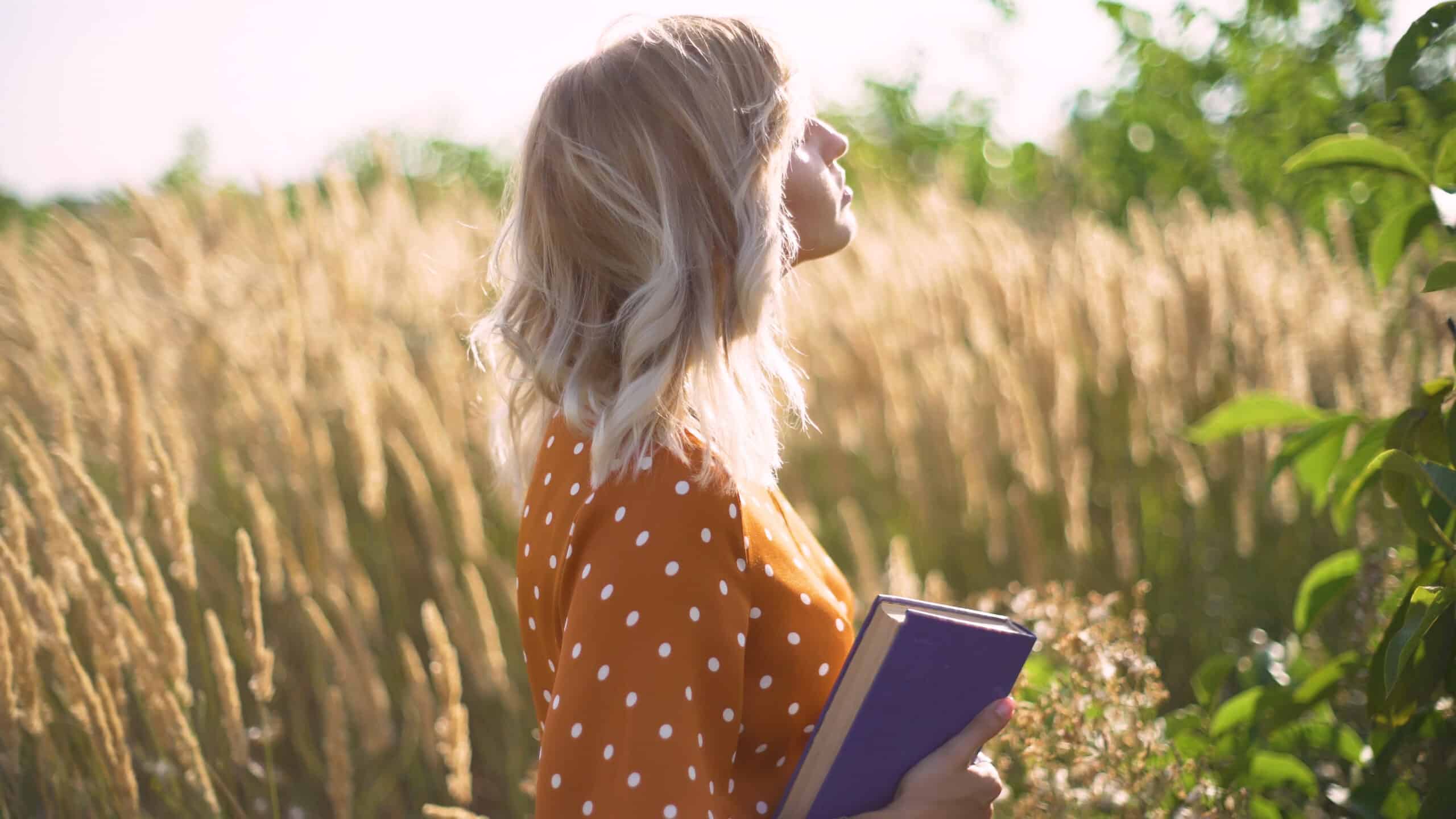 Beautiful happy woman carrying a purple book in a wheat field.