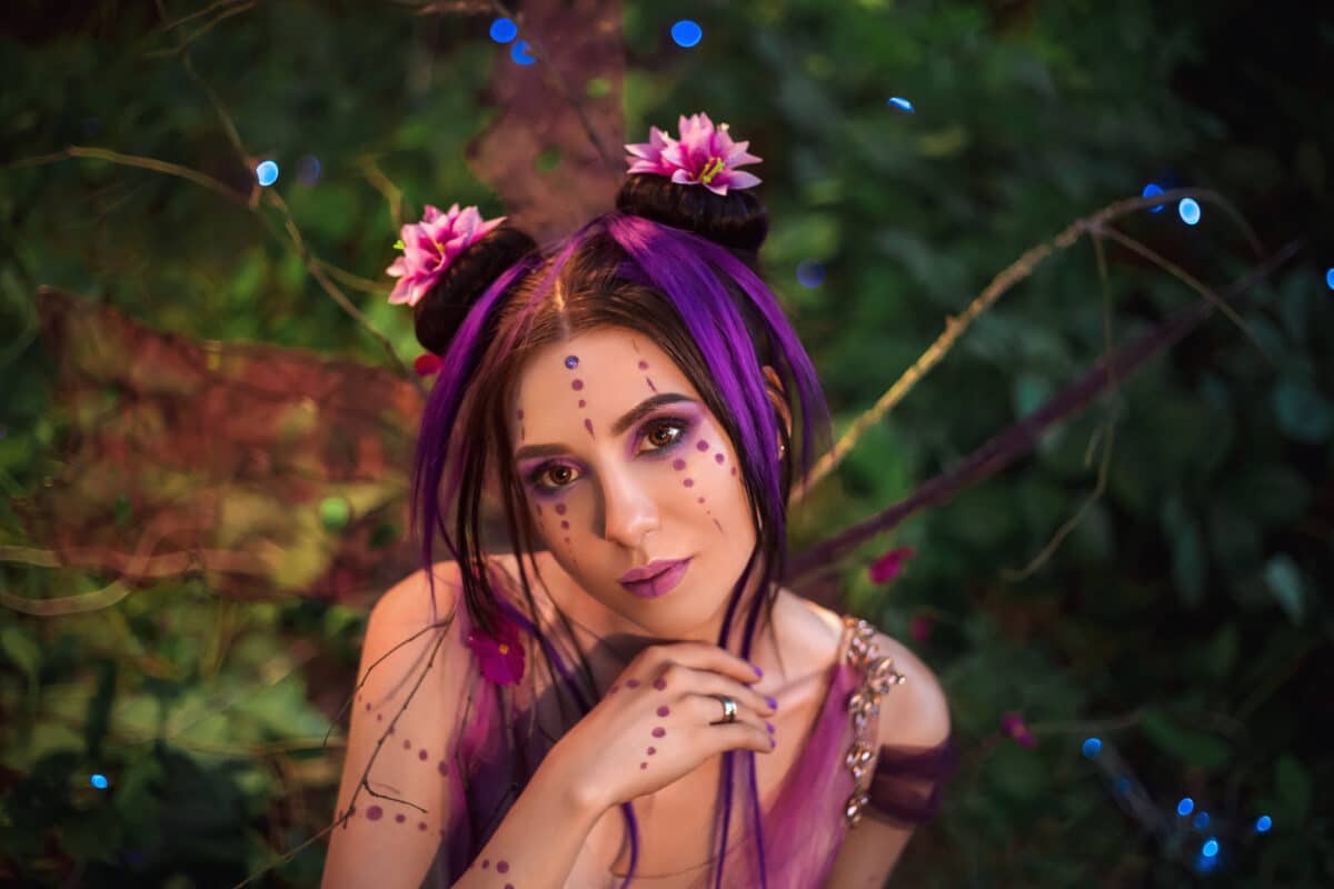 Fairy Coquette standing near the huge mushroom. Portrait, fairy looks into the camera her huge, beautiful eyes. The unusual fairy-tale image, purple dress and torn wings.