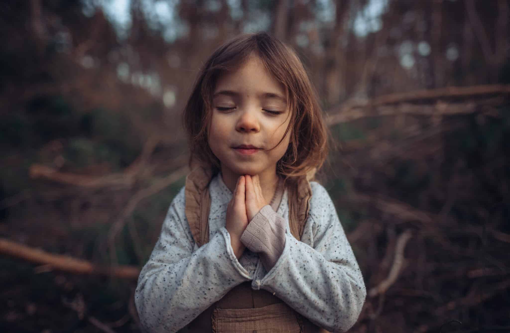 Happy little girl with closed eyes praying in autumn forest.