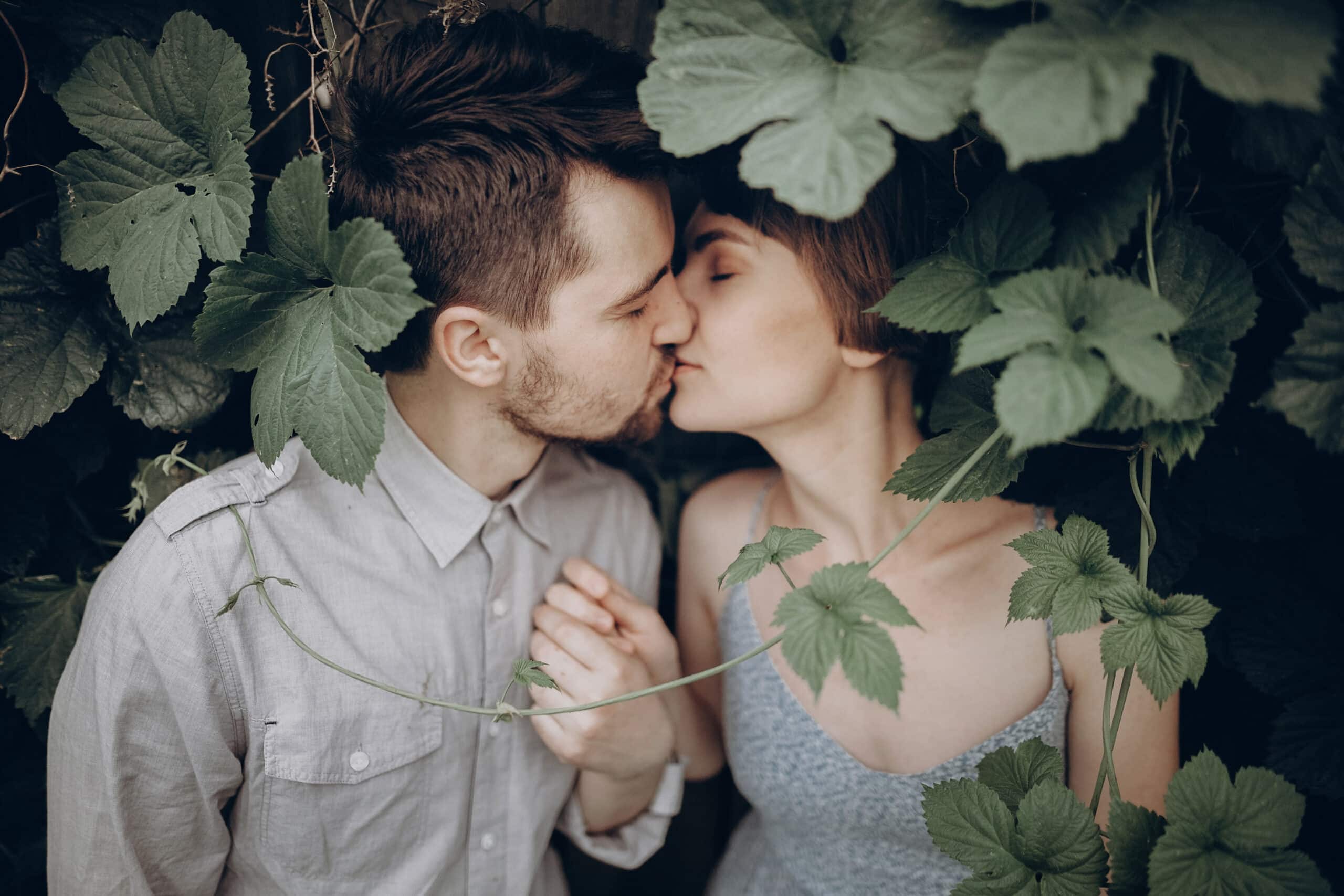 stylish hipster couple kissing in green leaves, holding hands