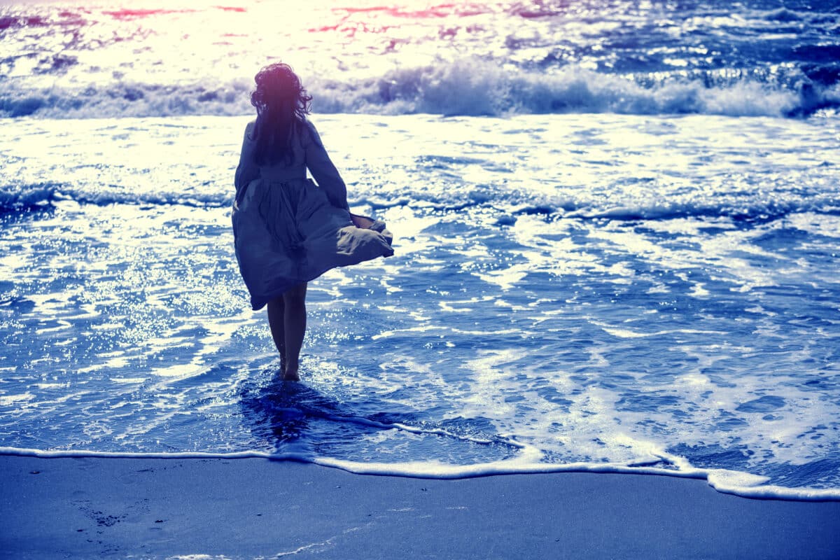 melancholic woman walks on the beach toward the sea 
