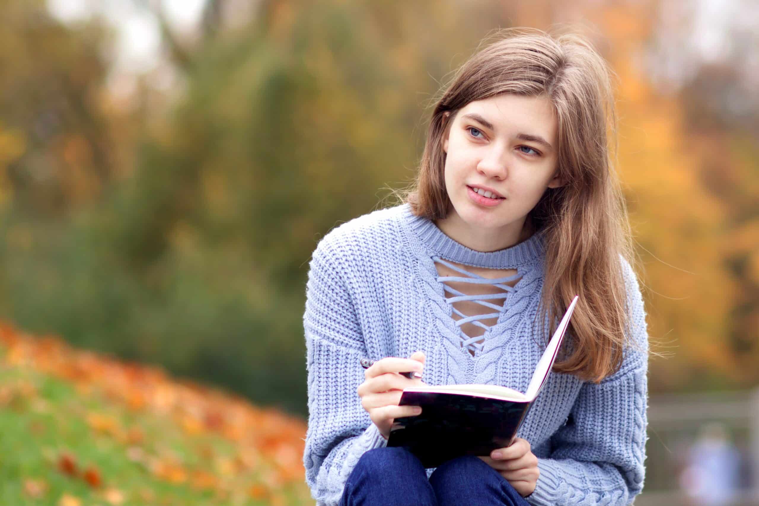 Young beautiful woman writing outdoors in golden autumn park.