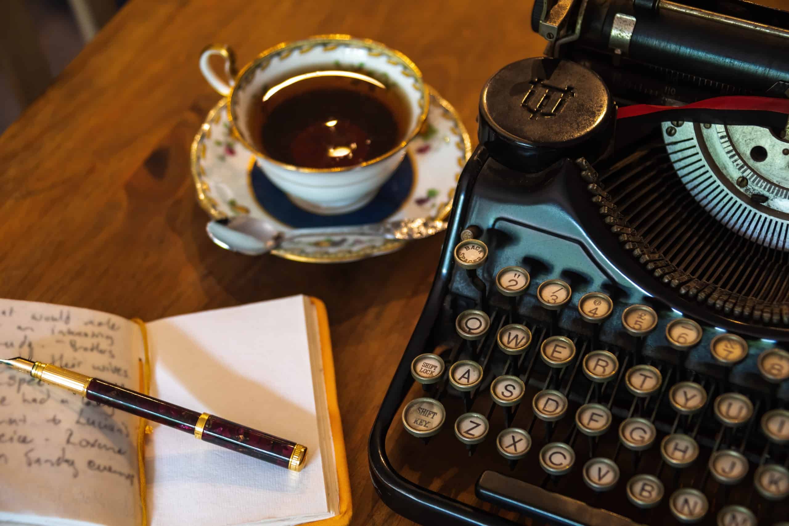 Vintage typewriter, a cup of tea, an open notebook, and pen.