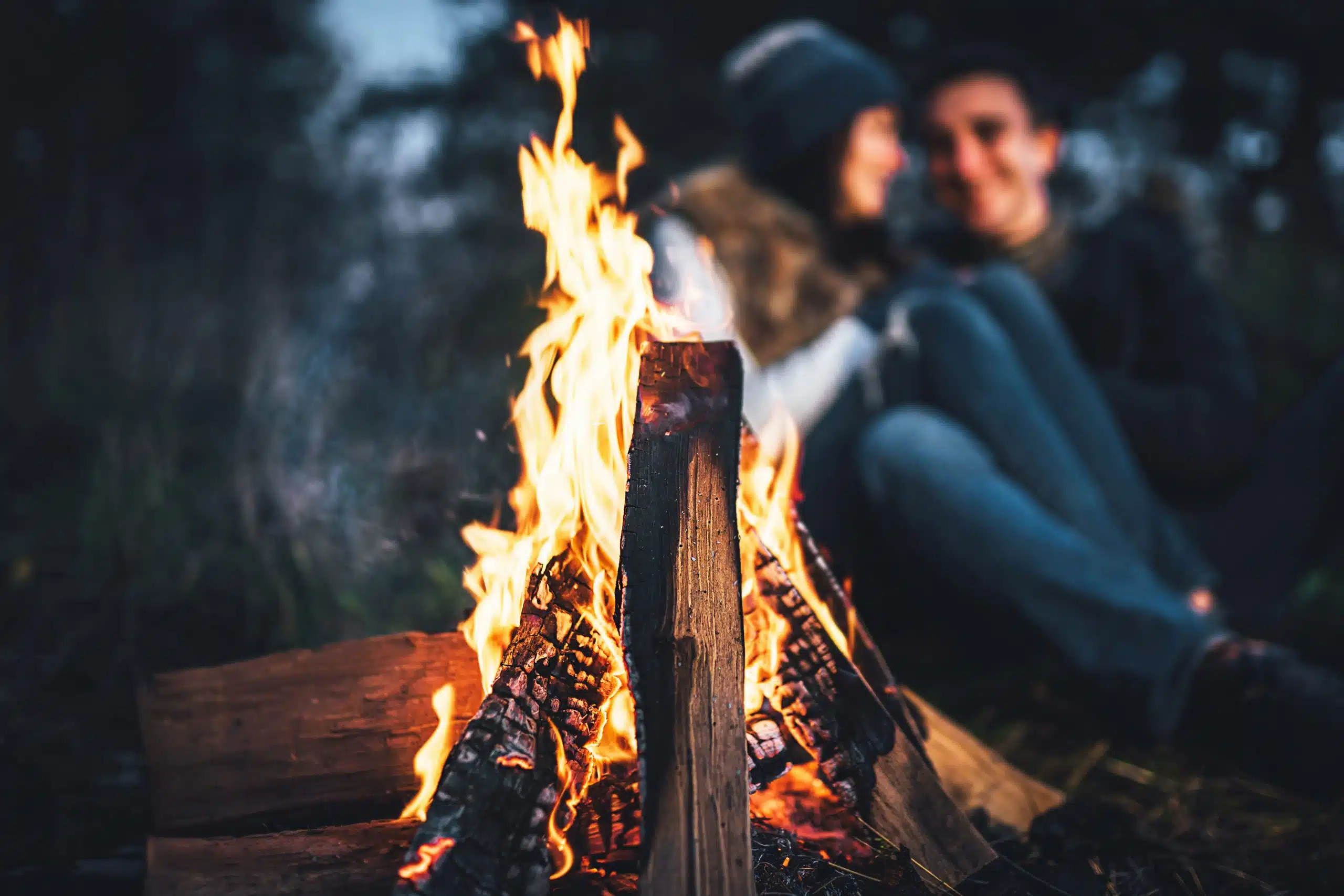 Couple relaxing near bonfire in the forest at night