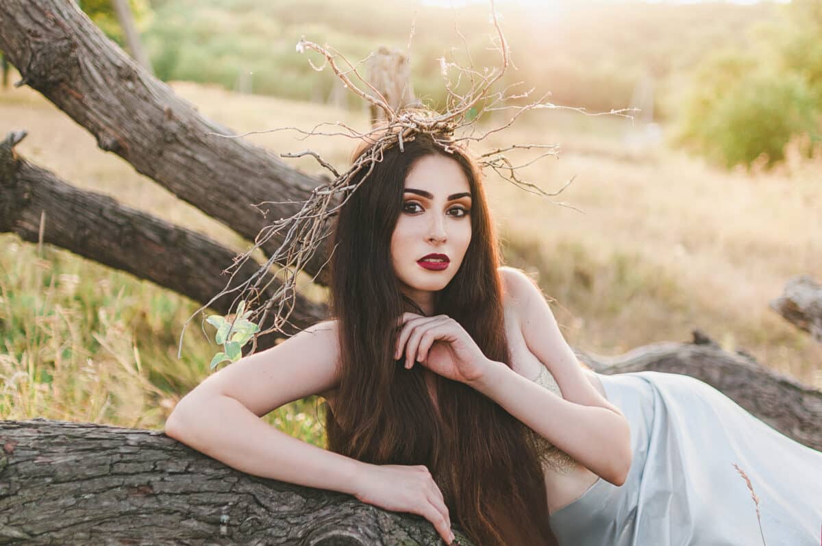 brunette girl Mavka Dryad Naiad forest nymph in a fairy tale in the forest among the trees in nature on her head a Hoop a wreath of branches dressed in a beige bra and silver fabric to the floor lying
