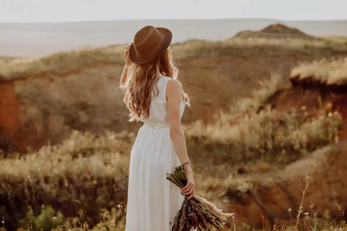 Woman in white dress holding flowers looking out to the mountains. 