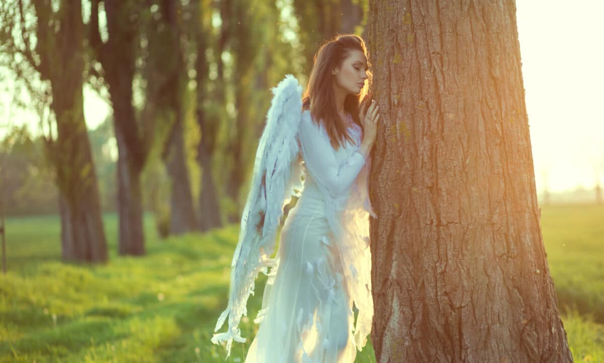 Pretty angel leaning against the tree