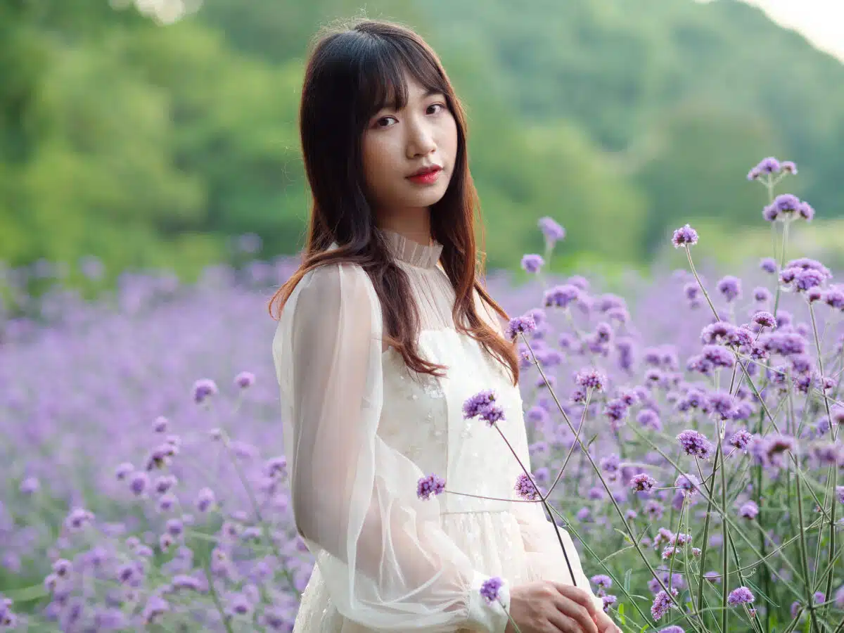 Beautiful woman in white dress posing among purple Verbena Bonariensis flower field, charming Chinese girl with black long hair enjoy her leisure time outdoor.