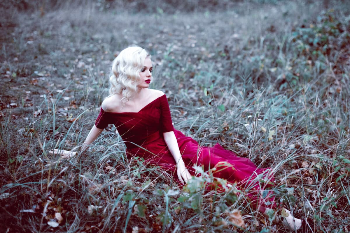 Fashion gorgeous young blonde woman in beautiful red dress in a fairy-tale forest. magic atmosphere.