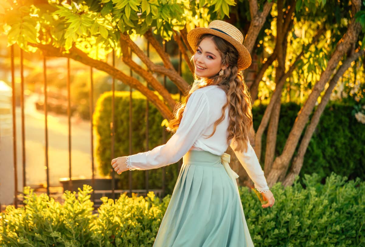 Art portrait happy woman dancing spinning in vintage straw hat on head, girl pretty smiling face red hair fly in wind, retro lady old style white blouse mint skirt. green tree sun light summer nature