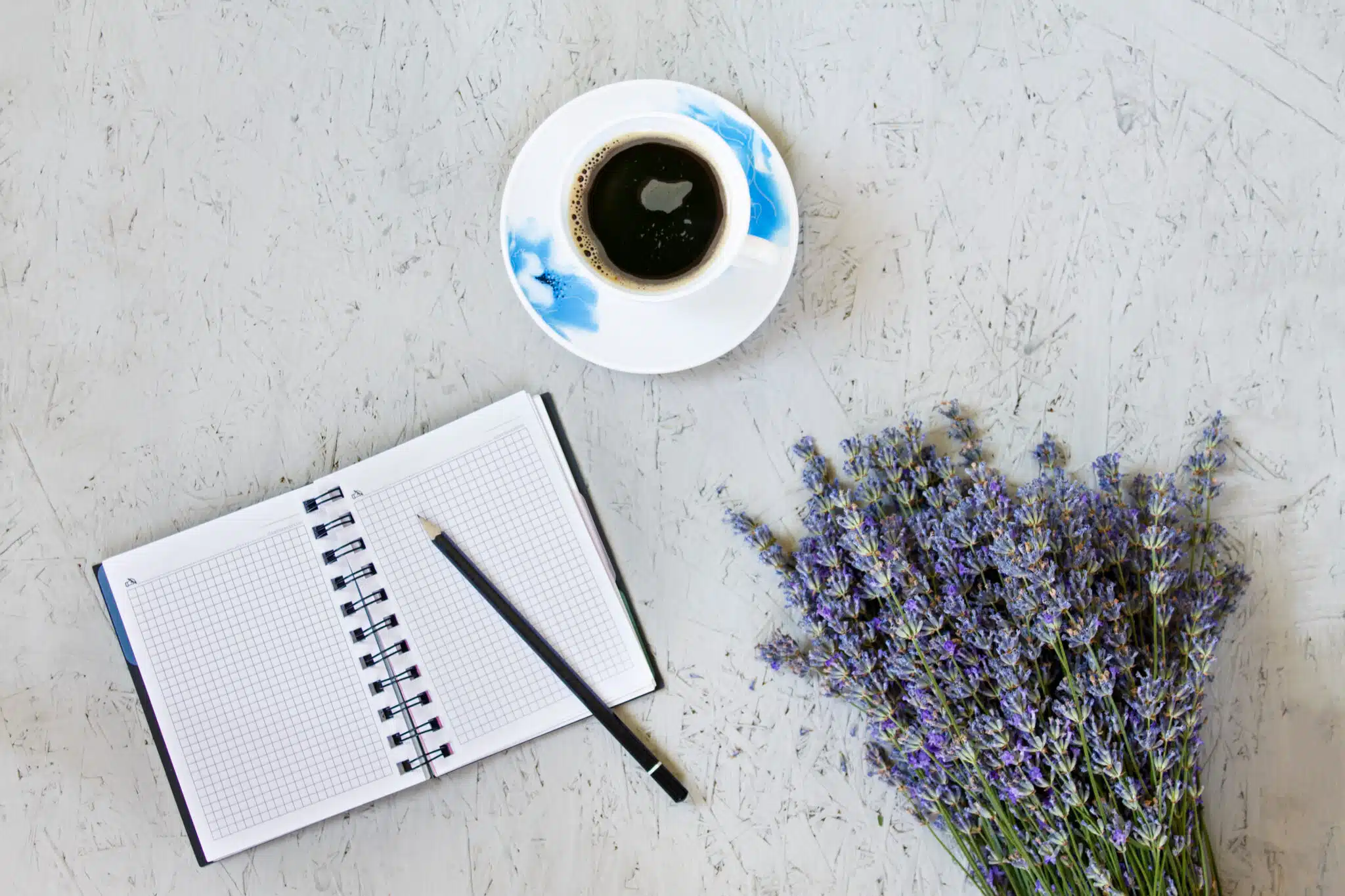 Morning coffee mug, blank notepad and purple lavender flowers on gray background, cozy summer breakfast, top view, flat lay