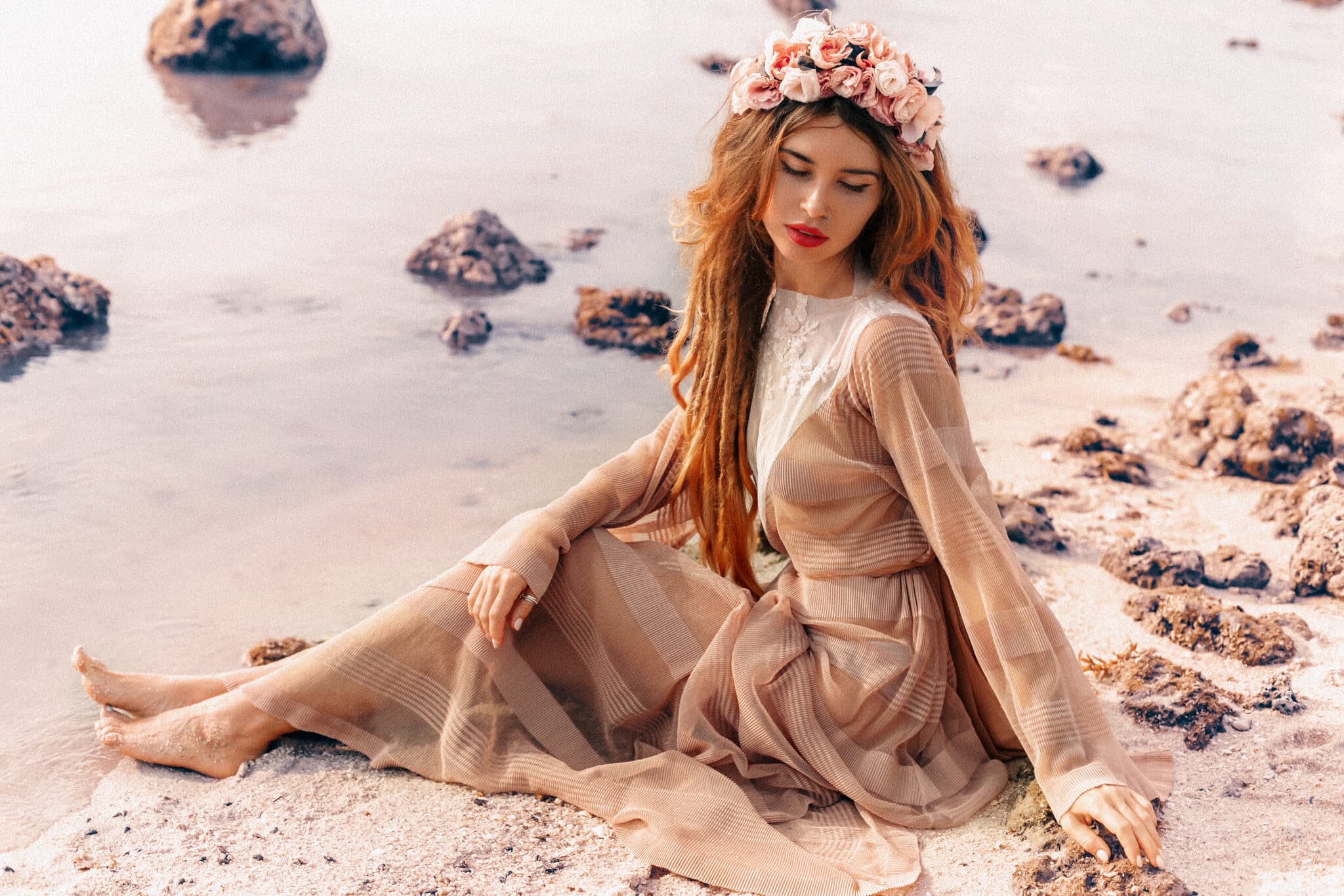 beautiful young woman in boho dress wears flower head wreath sits on the beach