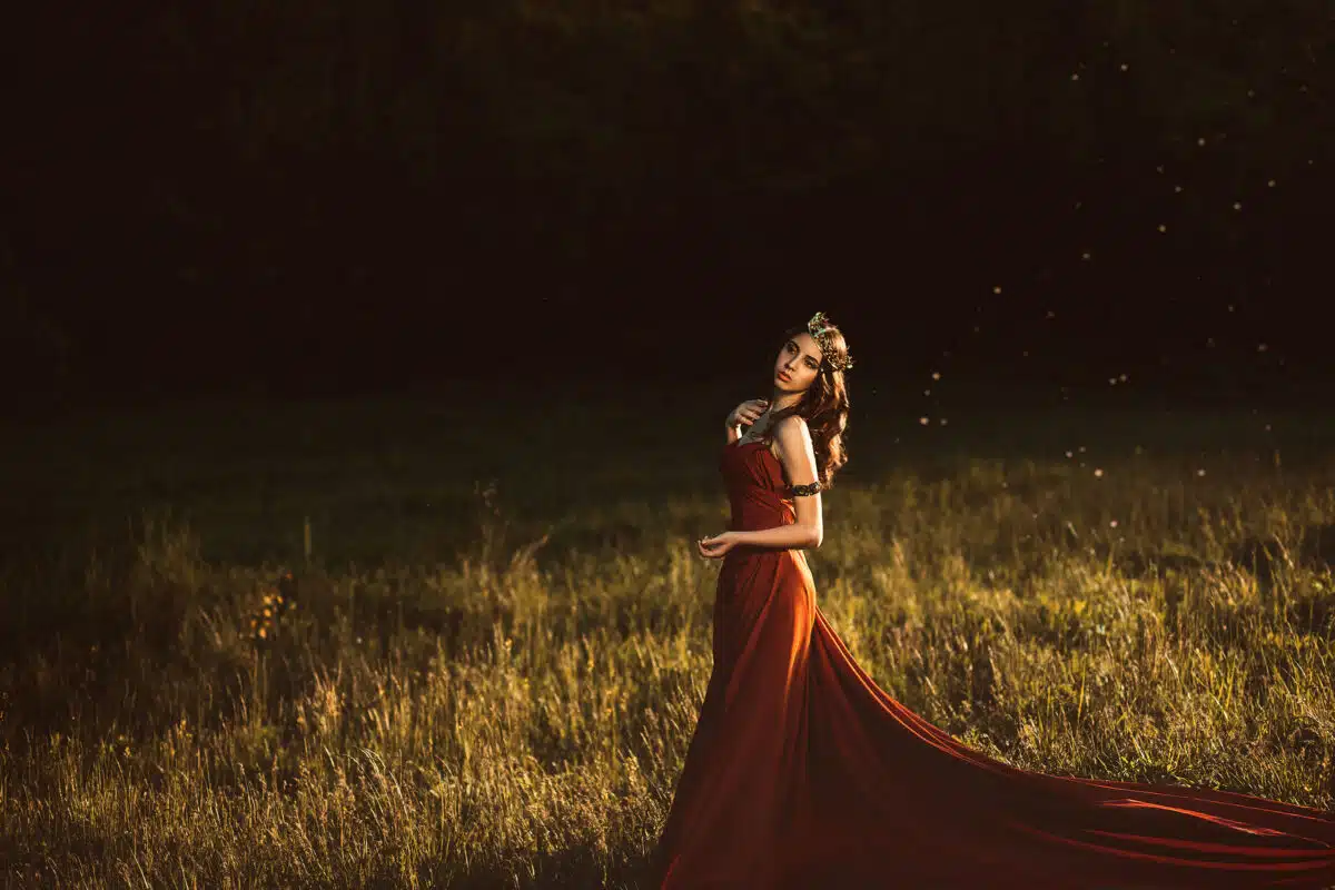 .Beautiful young princess in a long red dress walks among the green plants in the woods , a fashionable toning , creative color
