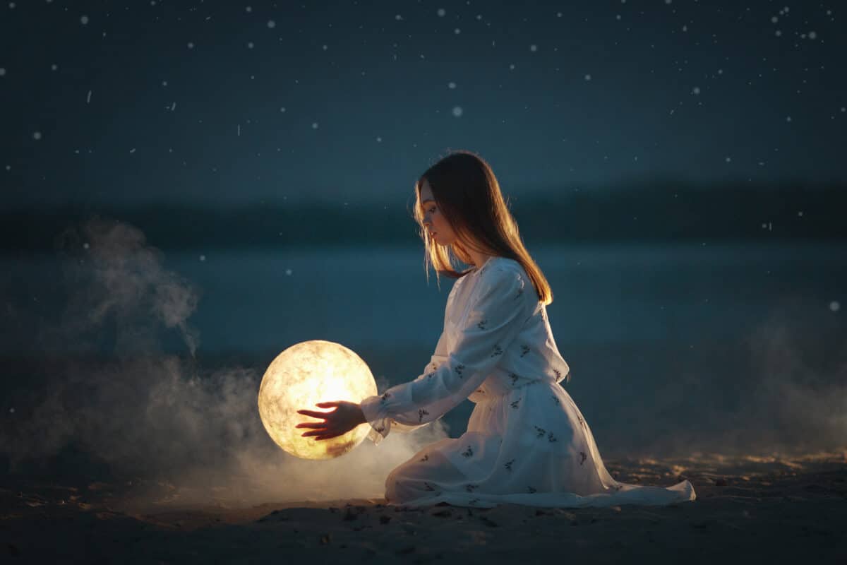 Beautiful attractive girl on a night beach with sand and stars hugs the moon