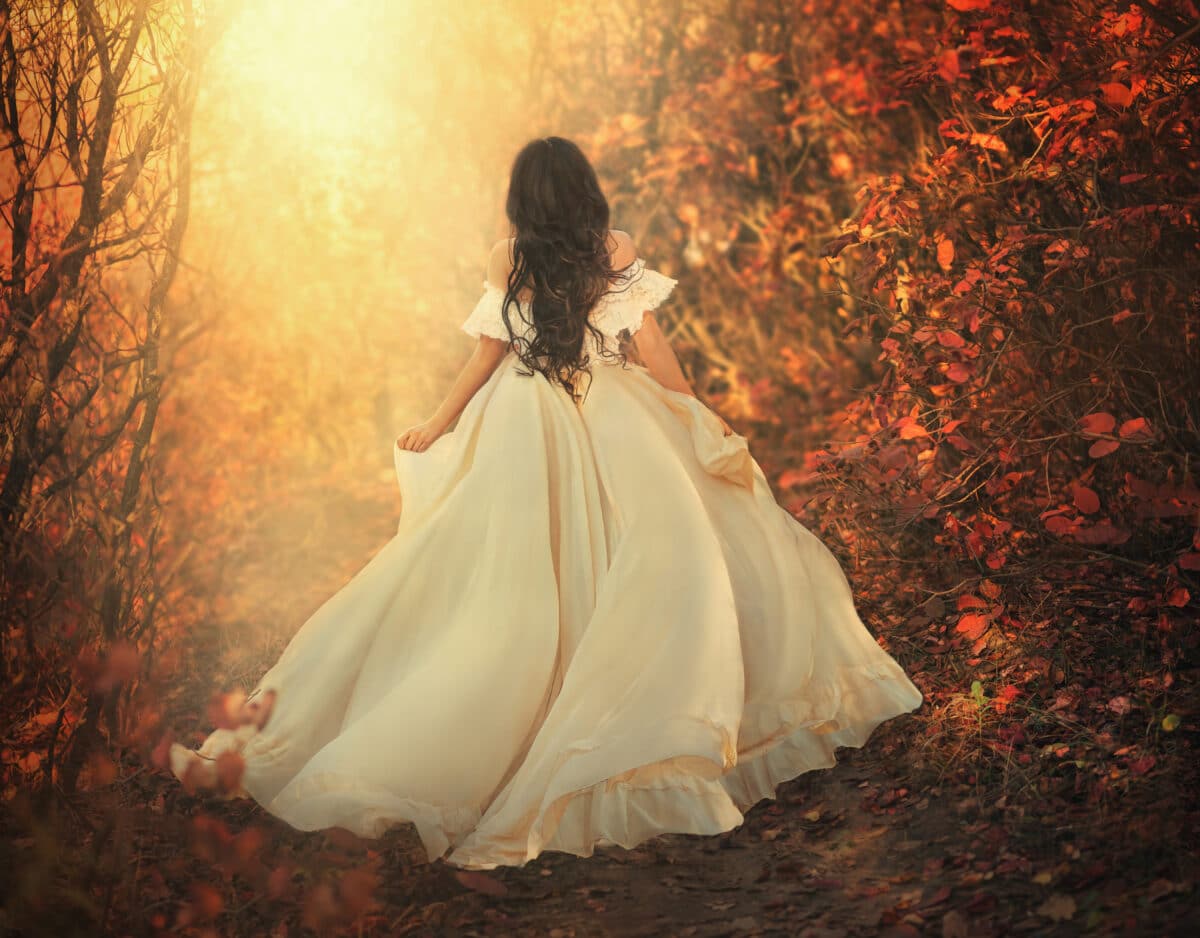 Art photo fantasy woman queen runs in dark autumn forest on magical sun light, long white vintage style dress flying waving wind motion. Girl princess sexy back bare open shoulders, no face. Red tree