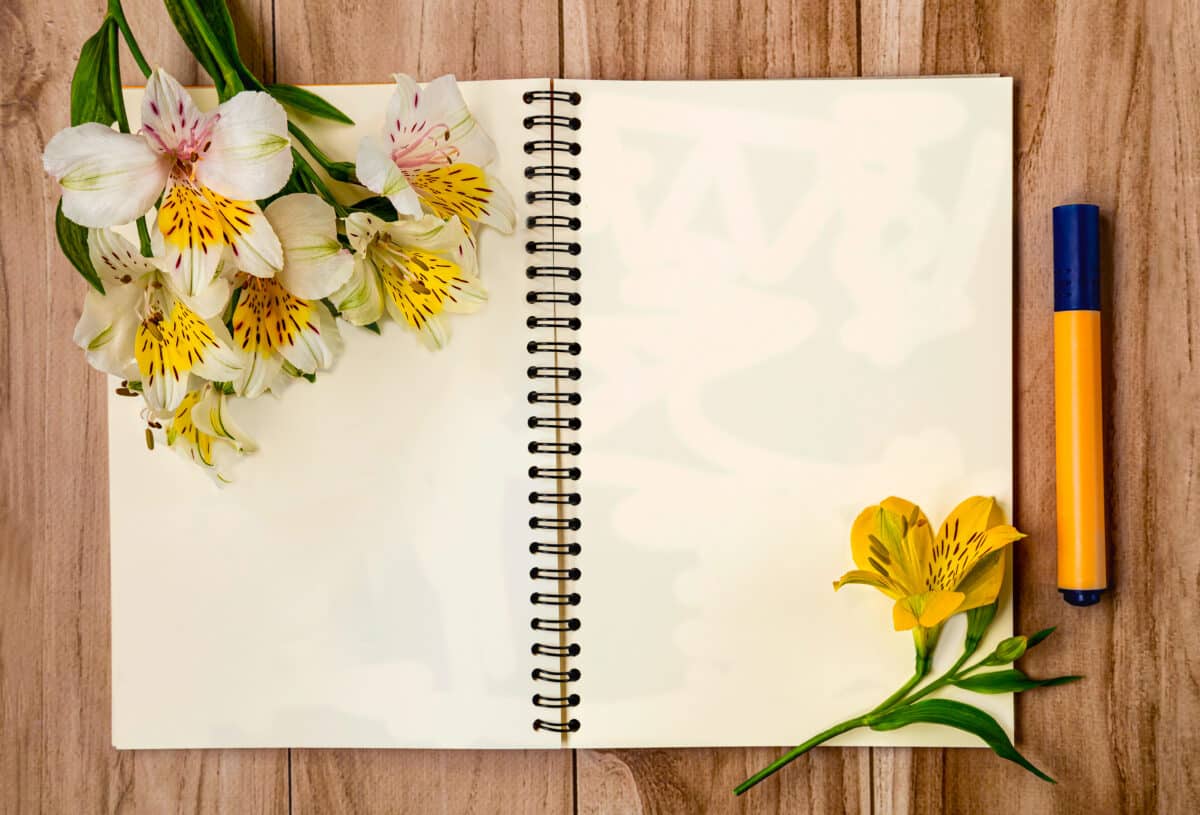 Top view of open notebook, marker and bouquet of alstroemeria flowers, white sheet of paper for text