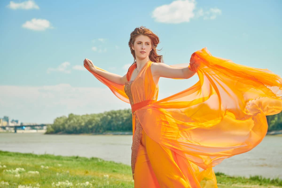 gorgeous elegant lady dressed in orange strolling by the river in summer