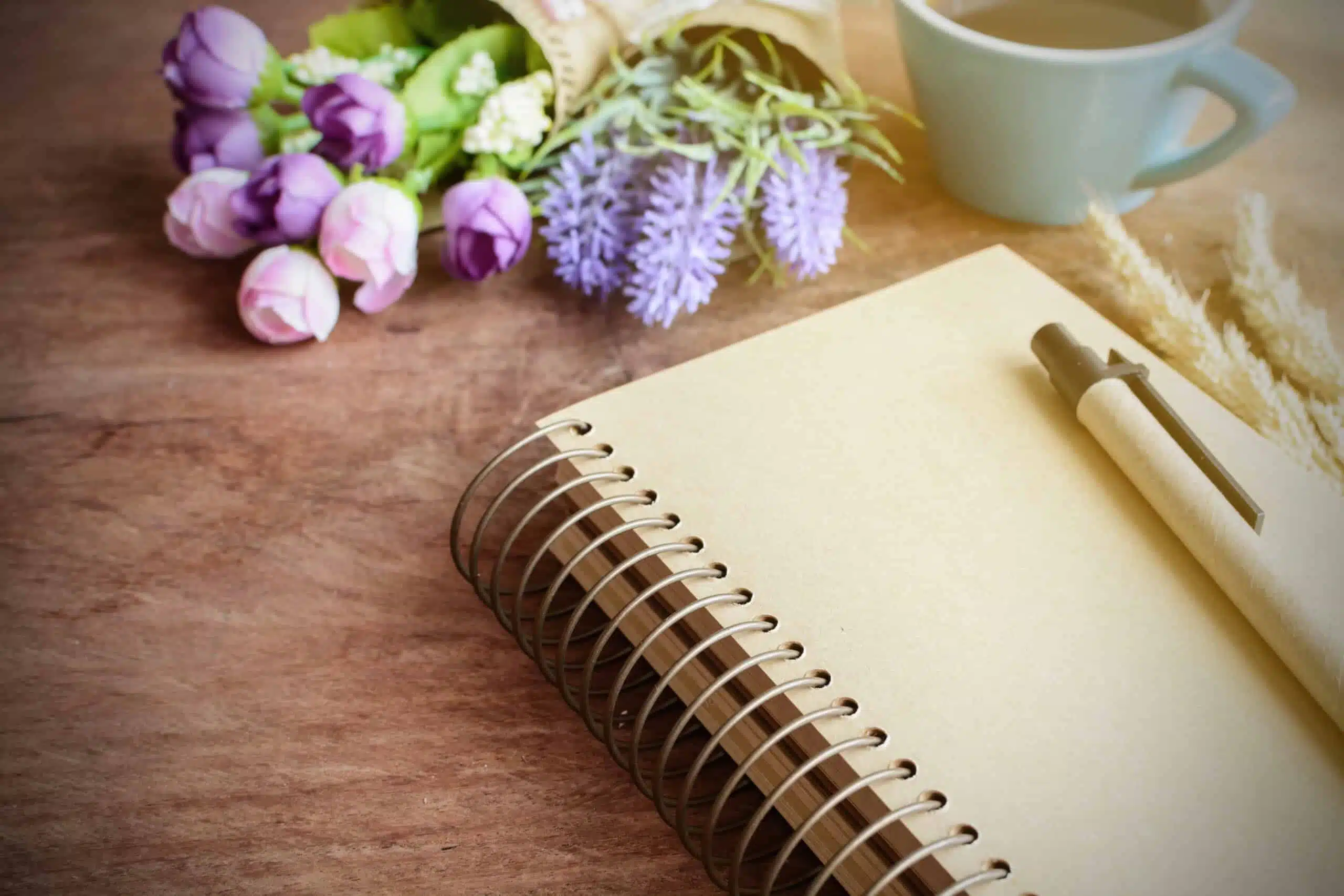 Cup of coffee with flower and blank notebook on wooden table