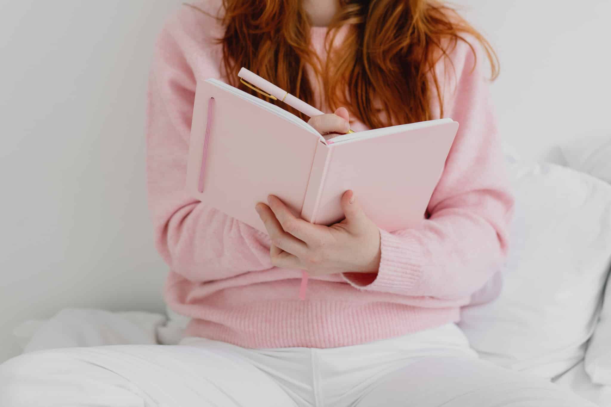 Cropped image of woman sitting on the bed and writing down in notebook.