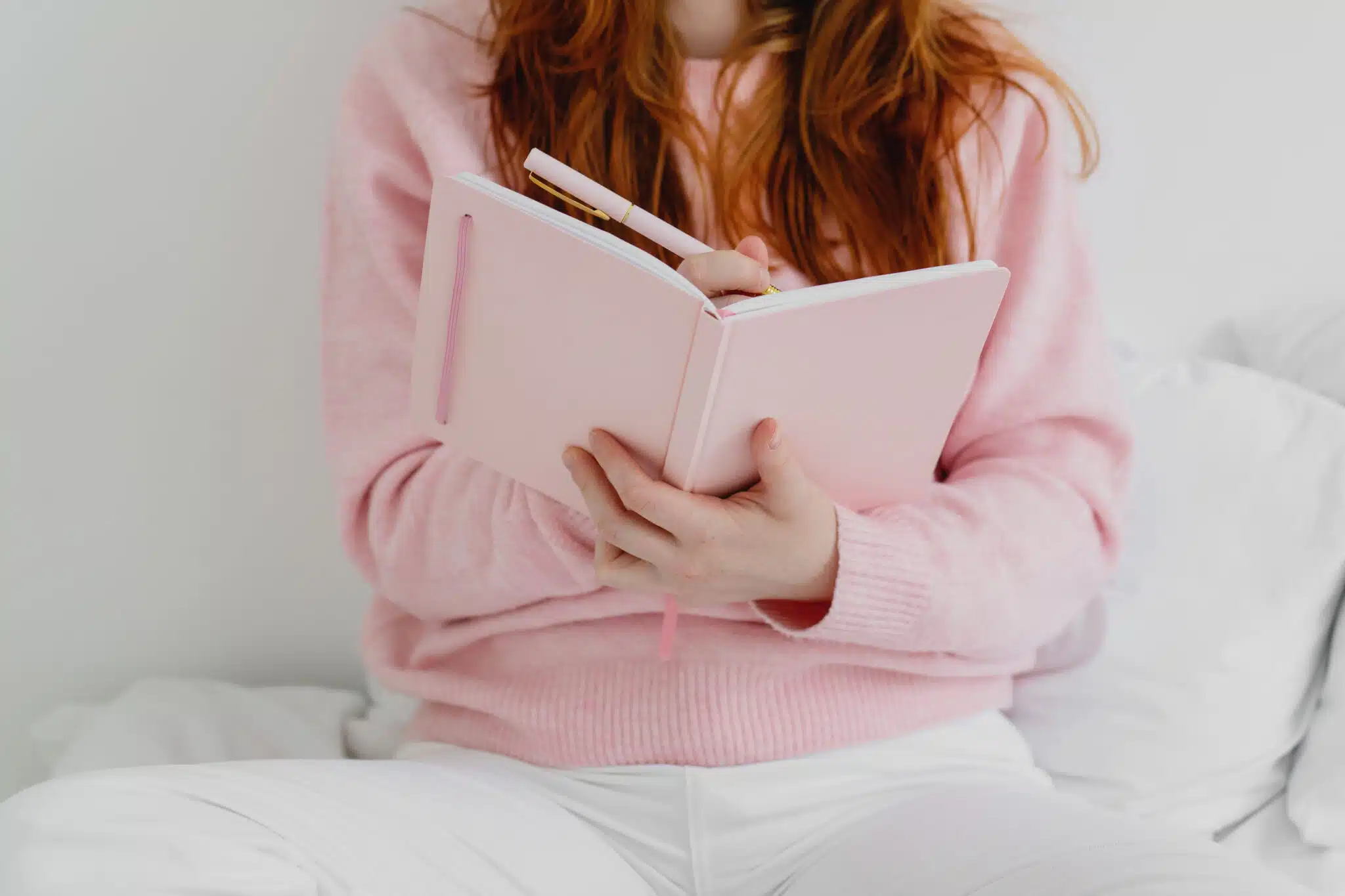 Cropped image of woman sitting on the bed and writing down in notebook.