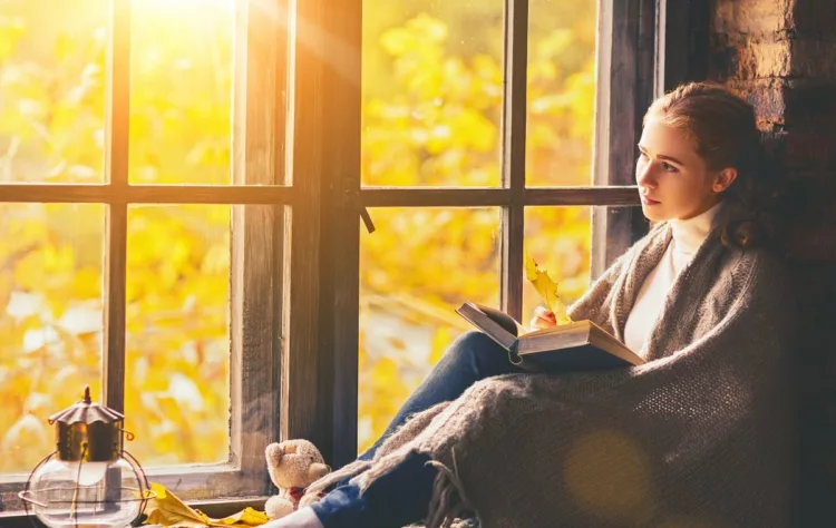 thoughtful woman reading book by the window in autumn