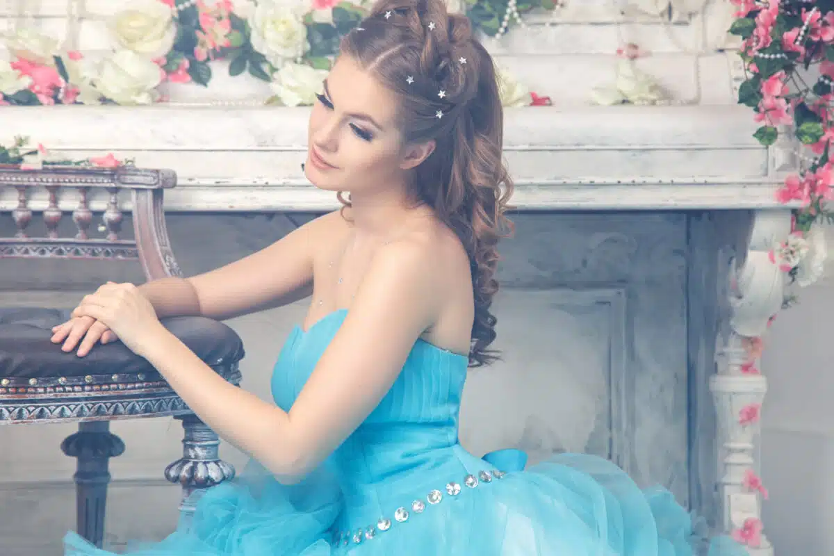 Beautiful young woman in gorgeous blue long dress sitting in a vintage room