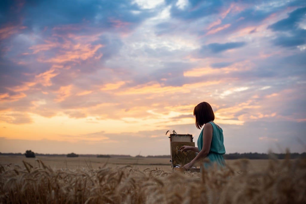 Female artist girl finishing her drawing at sunset in the middle of a wheat field.