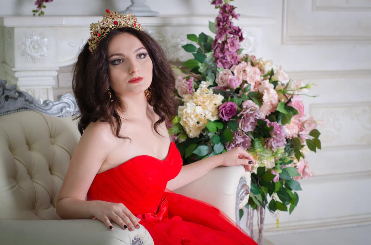 queen in in red long dress sitting on a white luxury chair