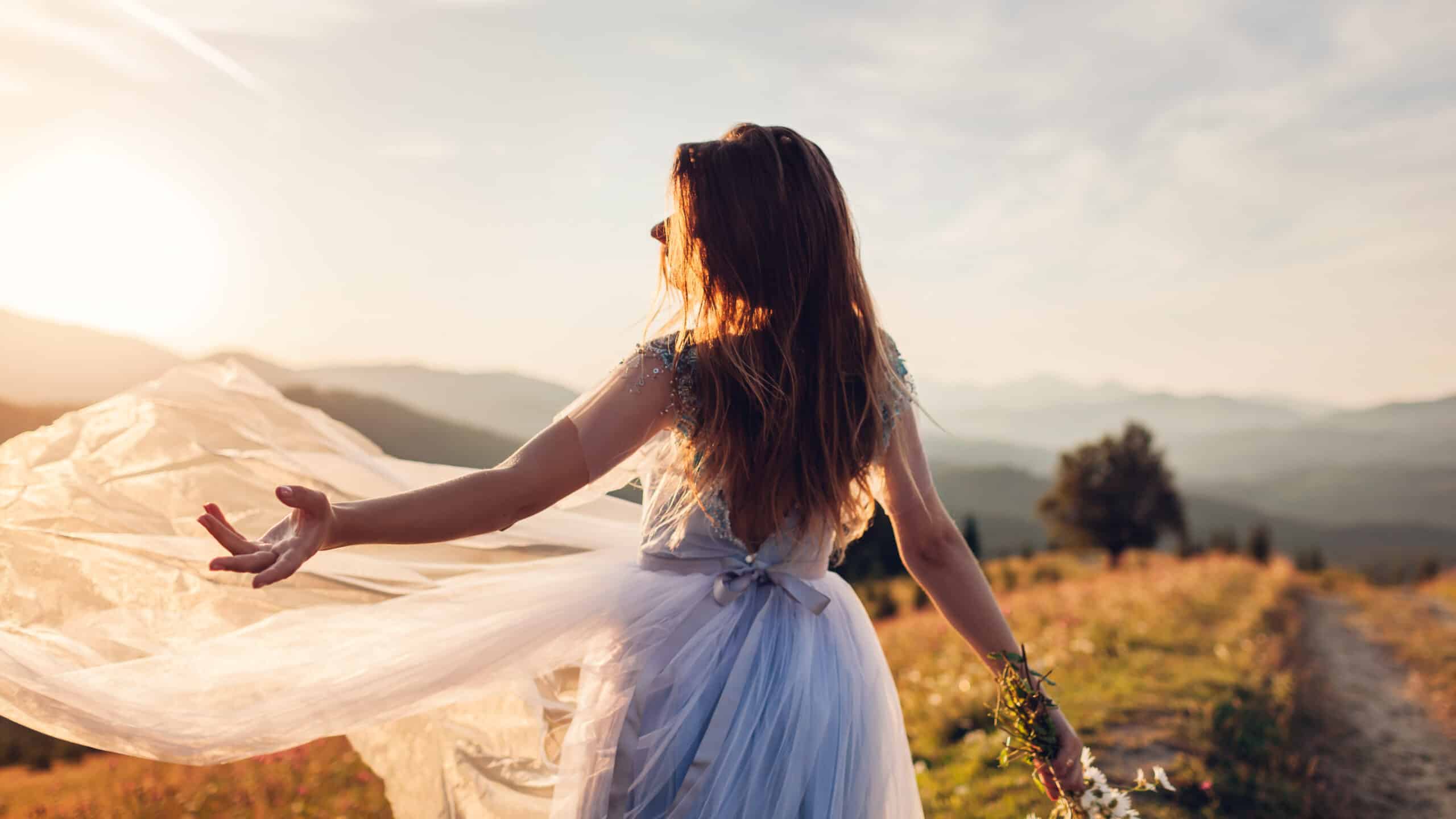 Beautiful bride dancing in blue wedding dress in mountains at sunset.