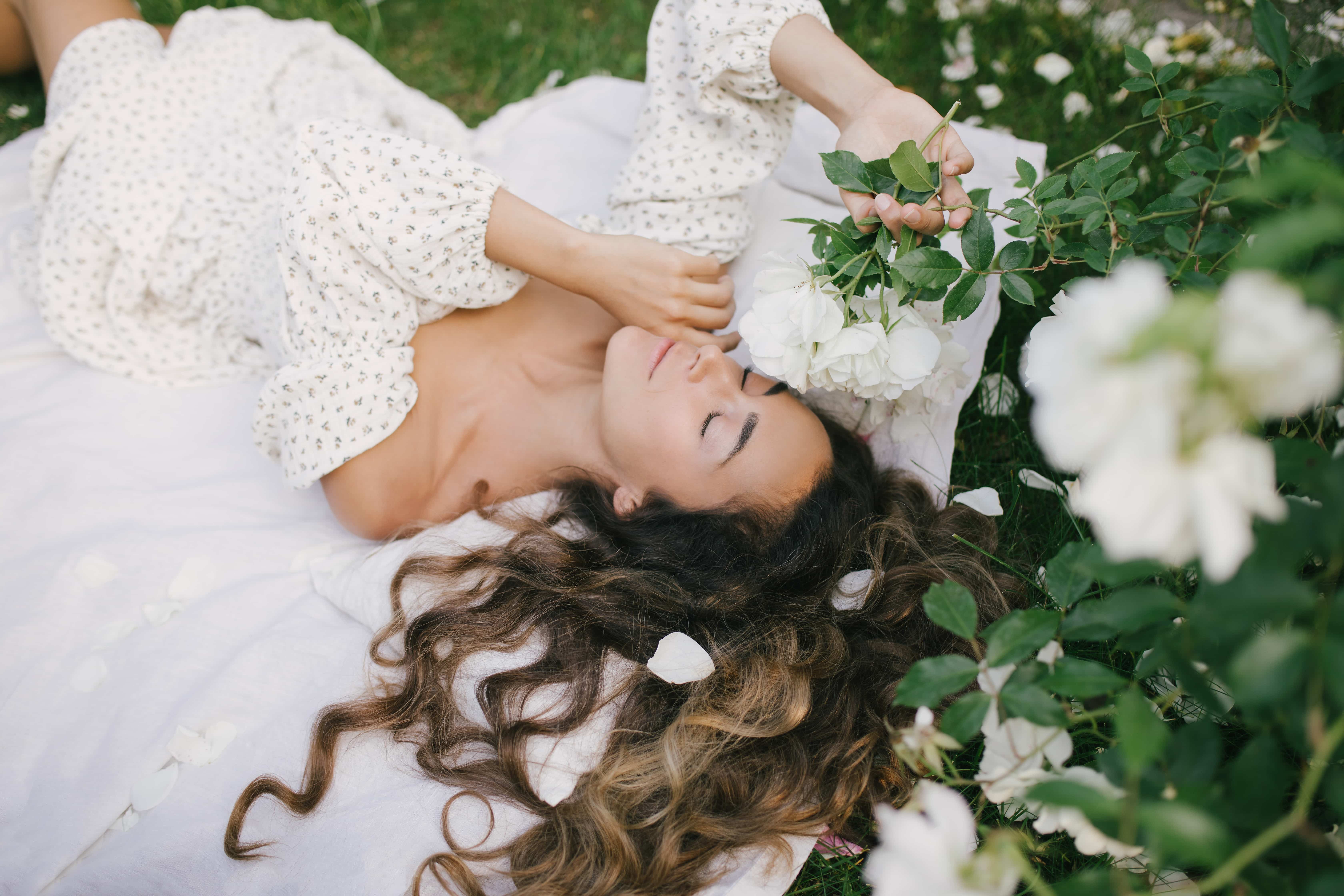 Young beautiful woman lying on the grass with long curly hair wearing white dress 