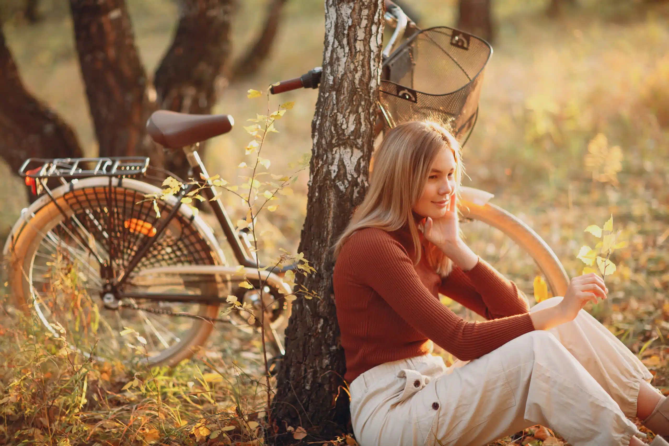 Happy young woman sitting with vintage bicycle in autumn park at sunset