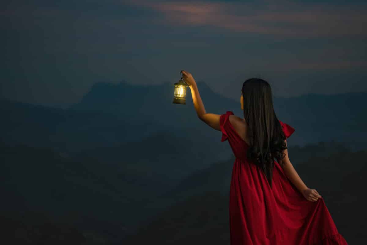 A woman standing with a lantern in the dark night on the mountain