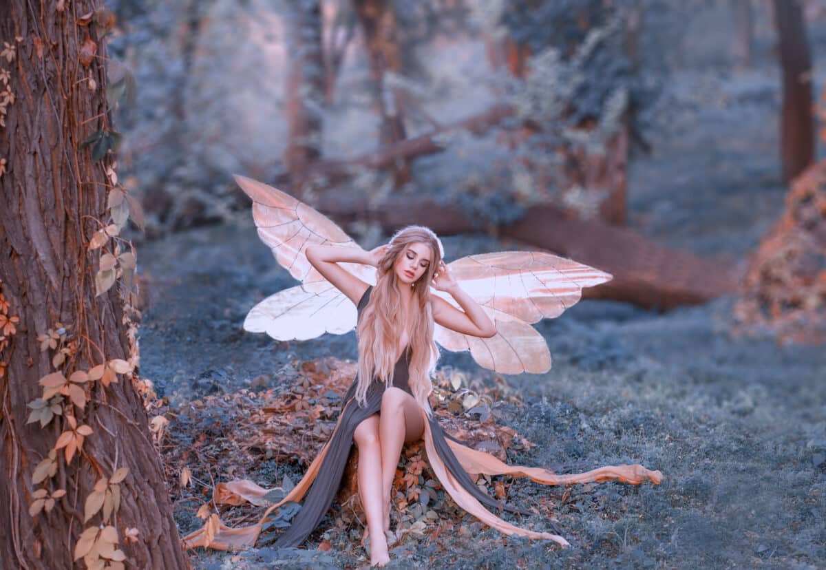 charming fairy woke up in forest, sweetly smacks after sleeping, cue girl with blond hair, eyes closed in long green dress with cut train, baby spirits with transparent butterfly wings