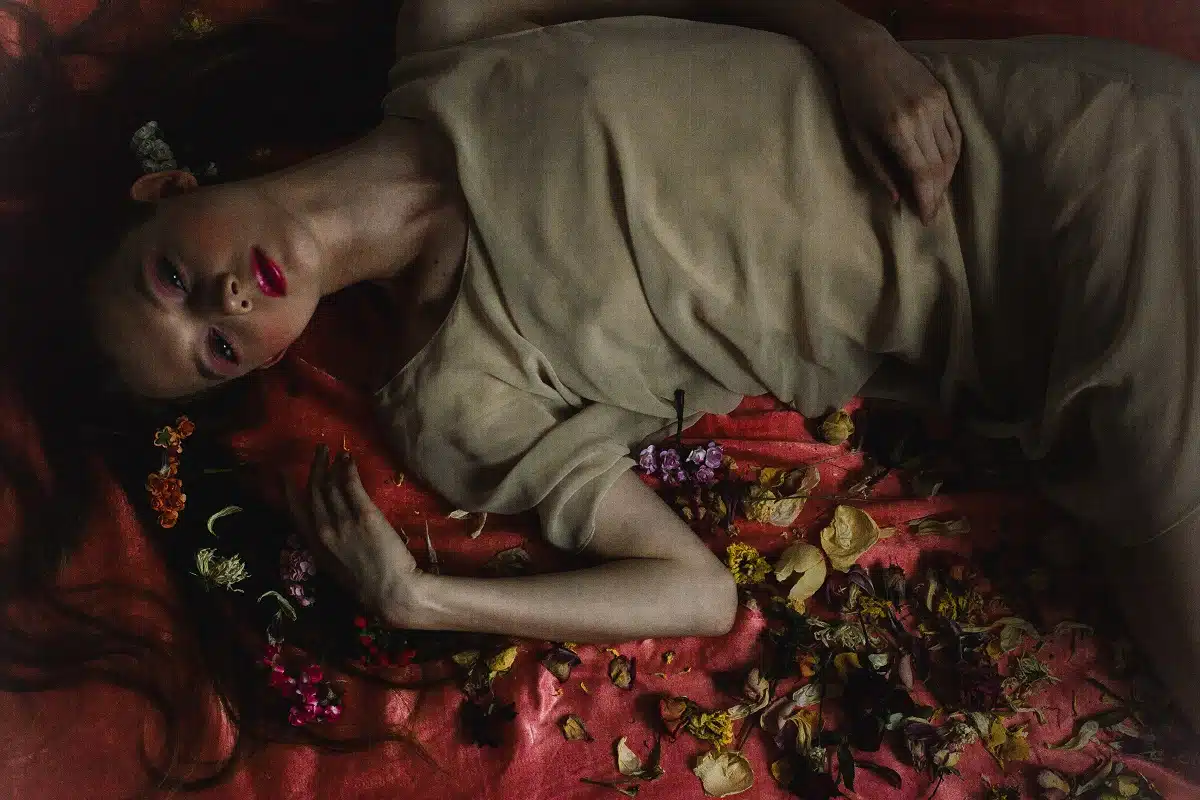 a beautiful but sad young lady lies in the petals in a long dress