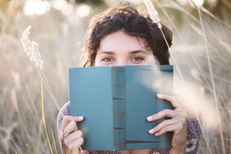Young woman reads a book in the grass field.