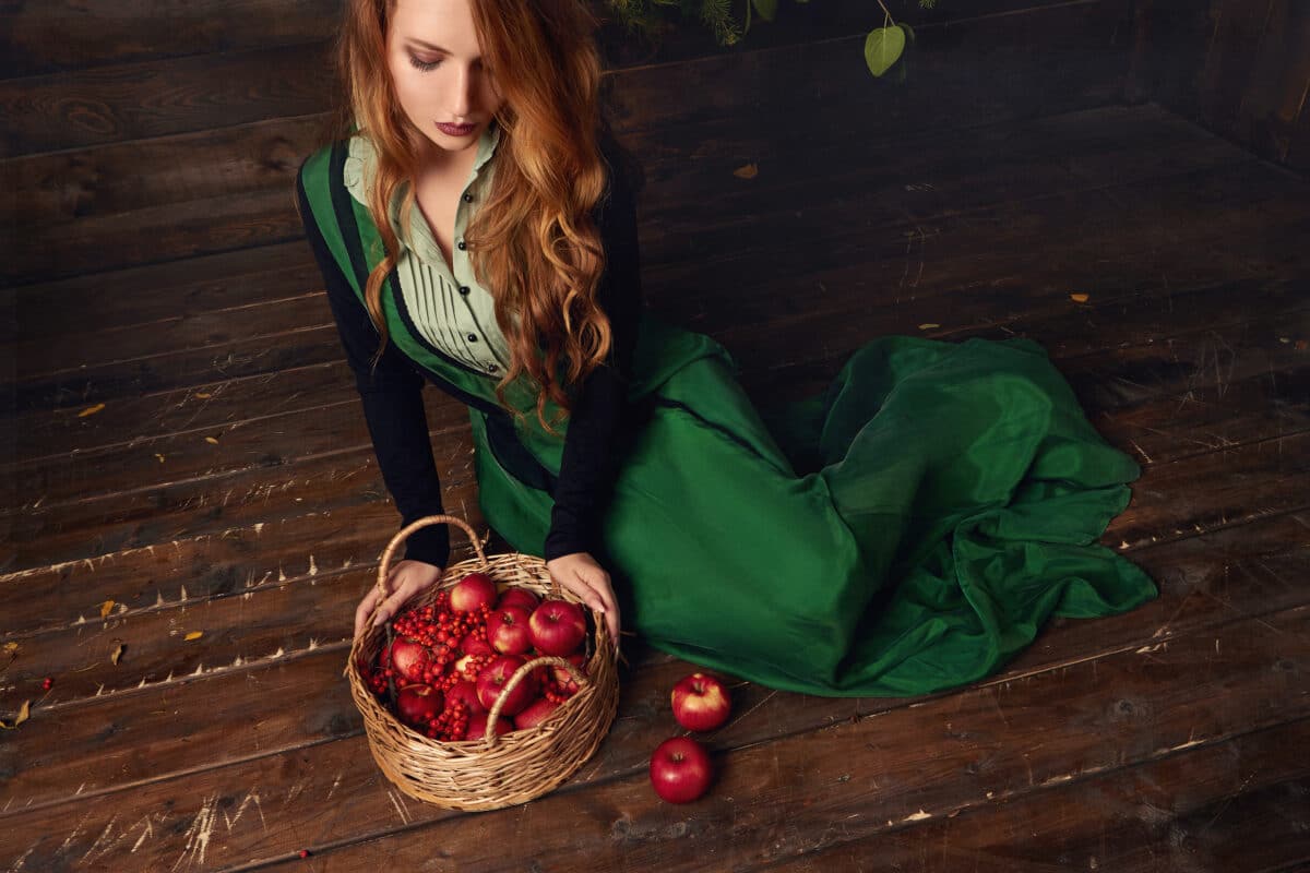 beautiful girl in vintage dress sits on the floor looking in the basket filled with cherries and apples