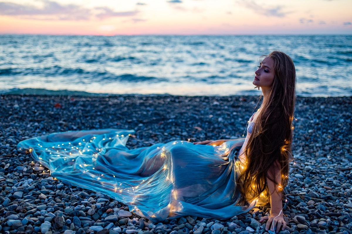 beautiful long haired woman in blue dress sitting on the beach
