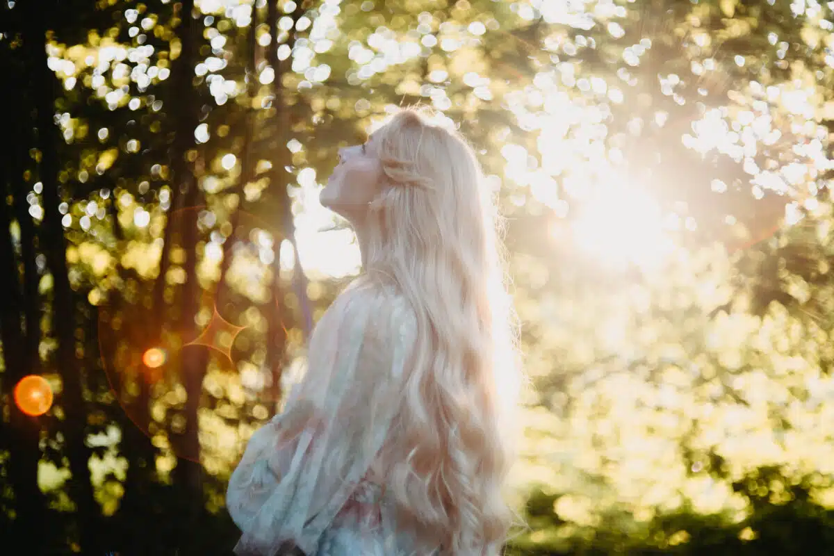 a divine beauty with long blond hair in nature facing the sun glare