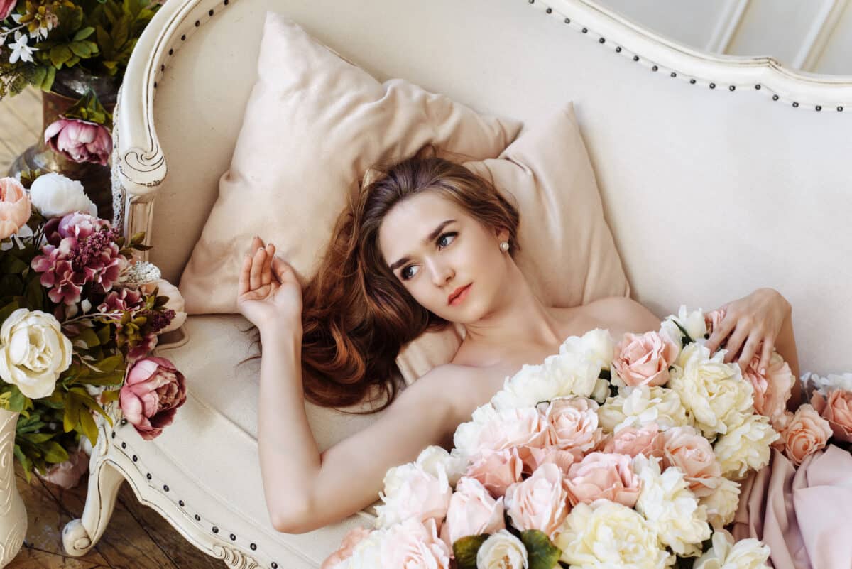 a beautiful lady in an elegant white dress of roses, peonies and flowers on a luxury sofa