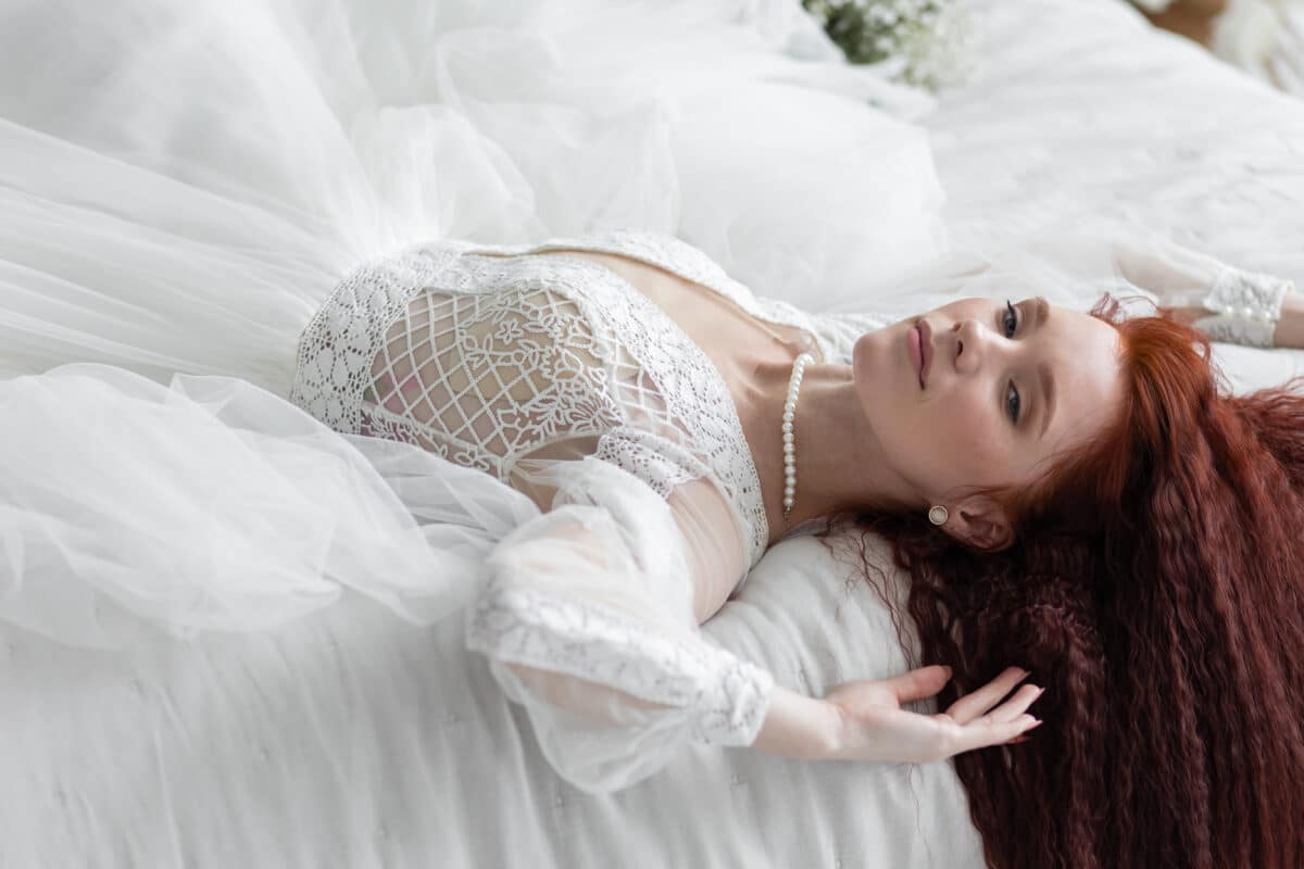 a beautiful redhead with long hair in a white lace dress lying on the bed