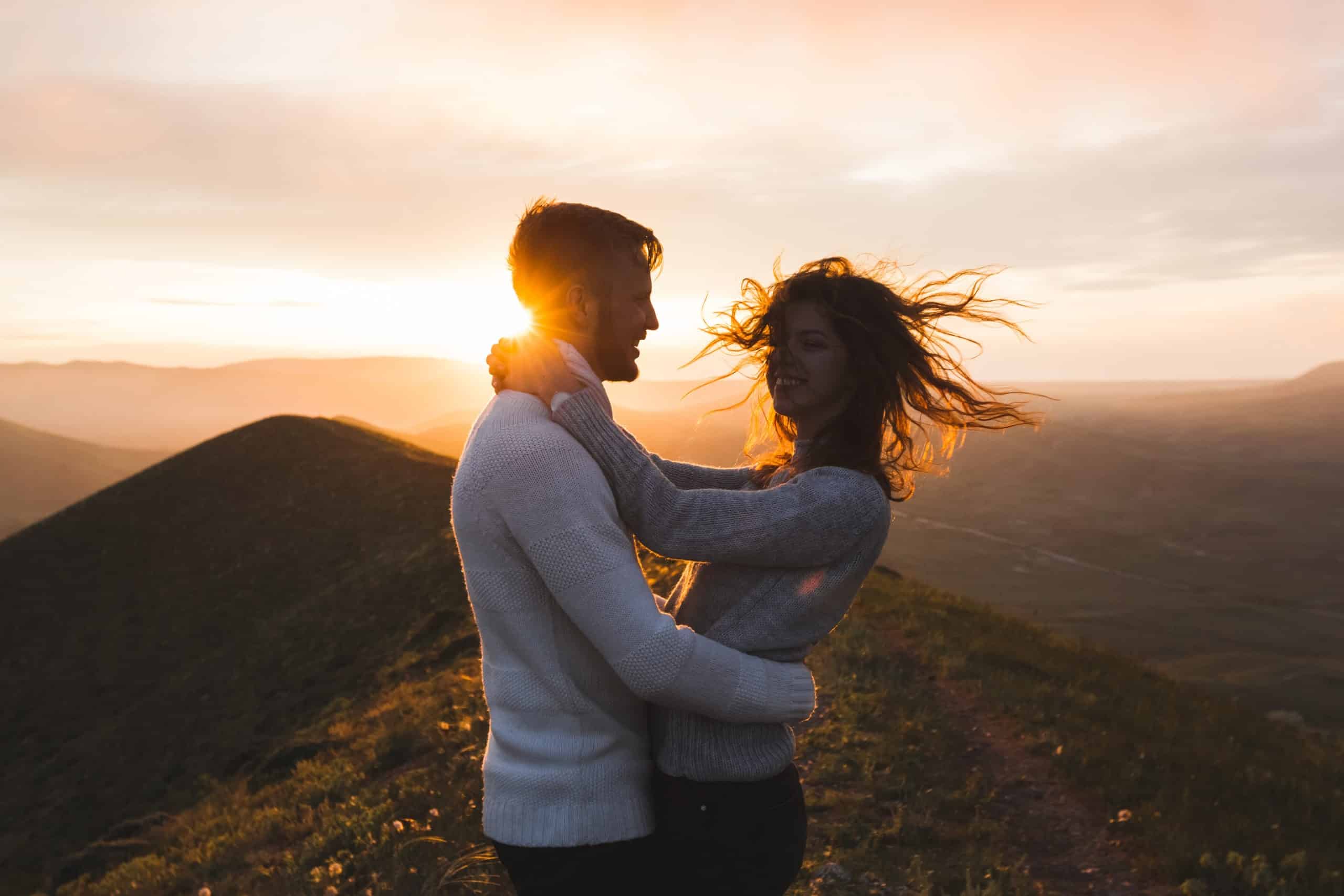 Happy couple hugging and kissing at sunset on mountain