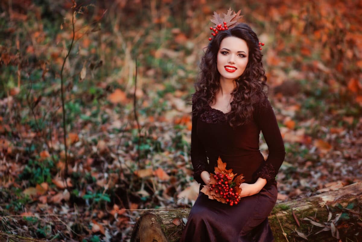 an autumn fairy sitting on a log with berries in her hands