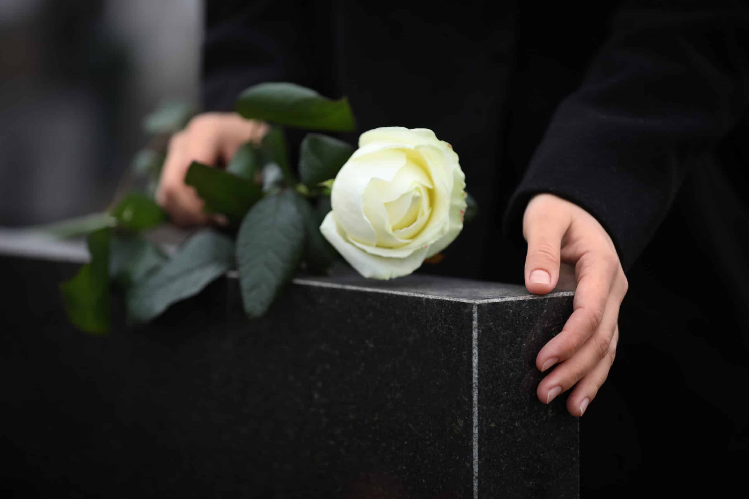 Woman holding white rose at a black granite tombstone.
