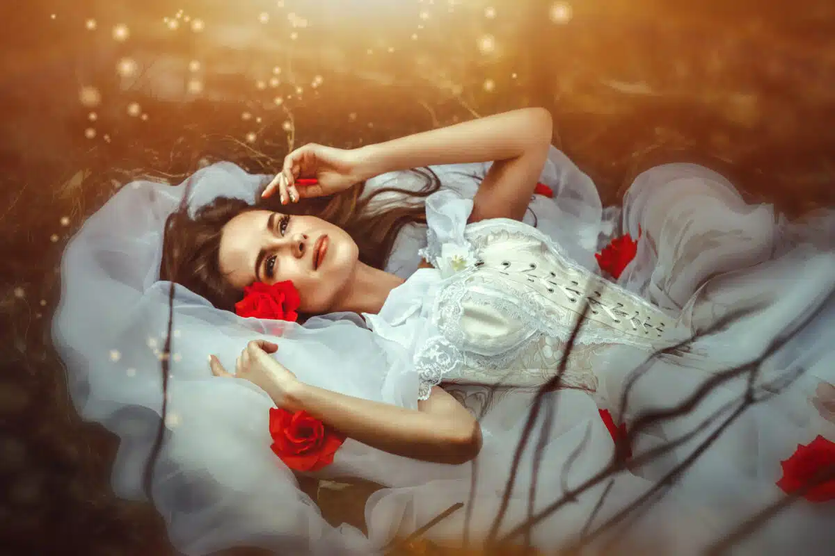 a sleeping beauty in a white dress lies on the bed with red roses 