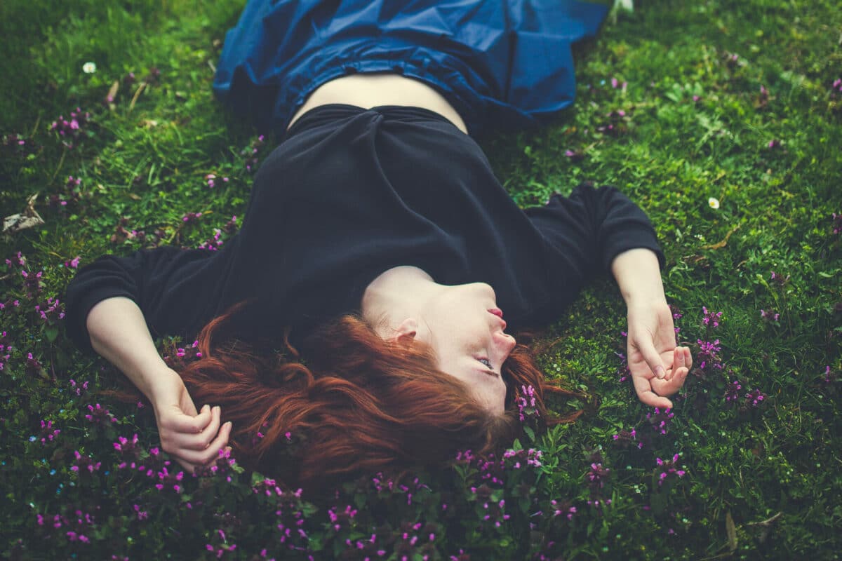 Beautiful redhead young woman lying on the grass with flowers