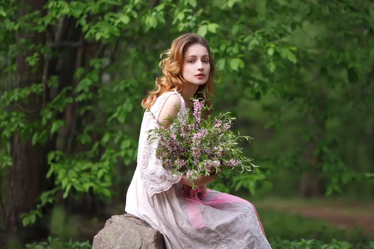 beautiful girl in a pink lace dress walks in the park with a bouquet of wildflowers