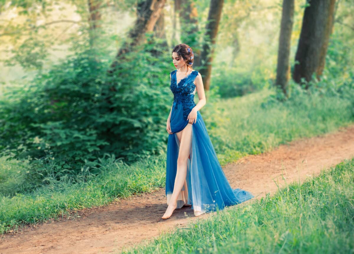 The girl in the evening, luxurious, watercolor dress, with a high slit. long legs. The image of the party, a young charming graduate. Collected hairstyle with weaves, hair decorated with blue flowers