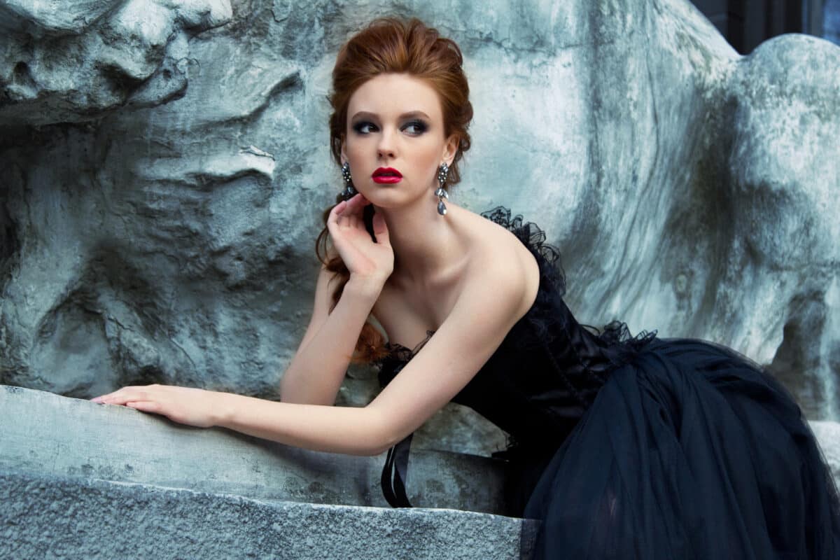 a beautiful young gothic woman in a black dress sitting near the castle