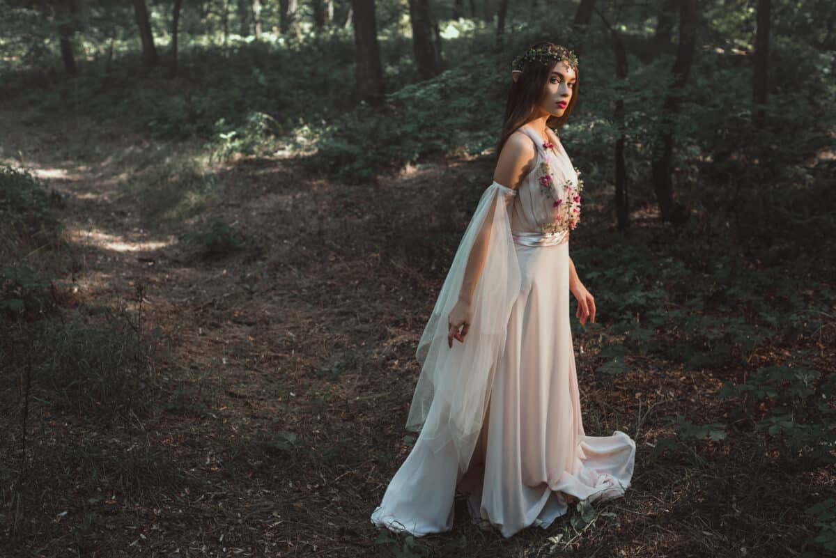 elegant mystic elf in dress with flowers walking in forest